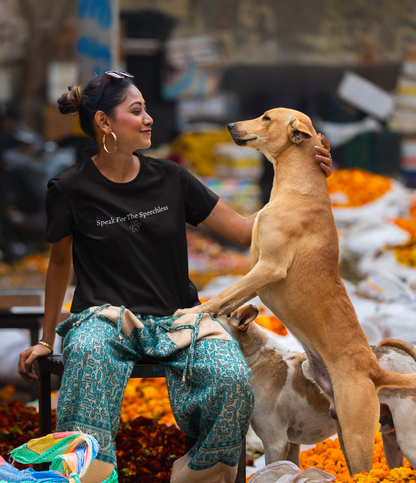 Woman sitting with a dog at a market stall selling flowers and fruits with a tshirt saying 'speak for the speechless'.