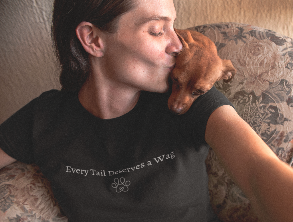 Person wearing a shirt with 'Every Tail Deserves a Wag' on a floral couch with a dog.