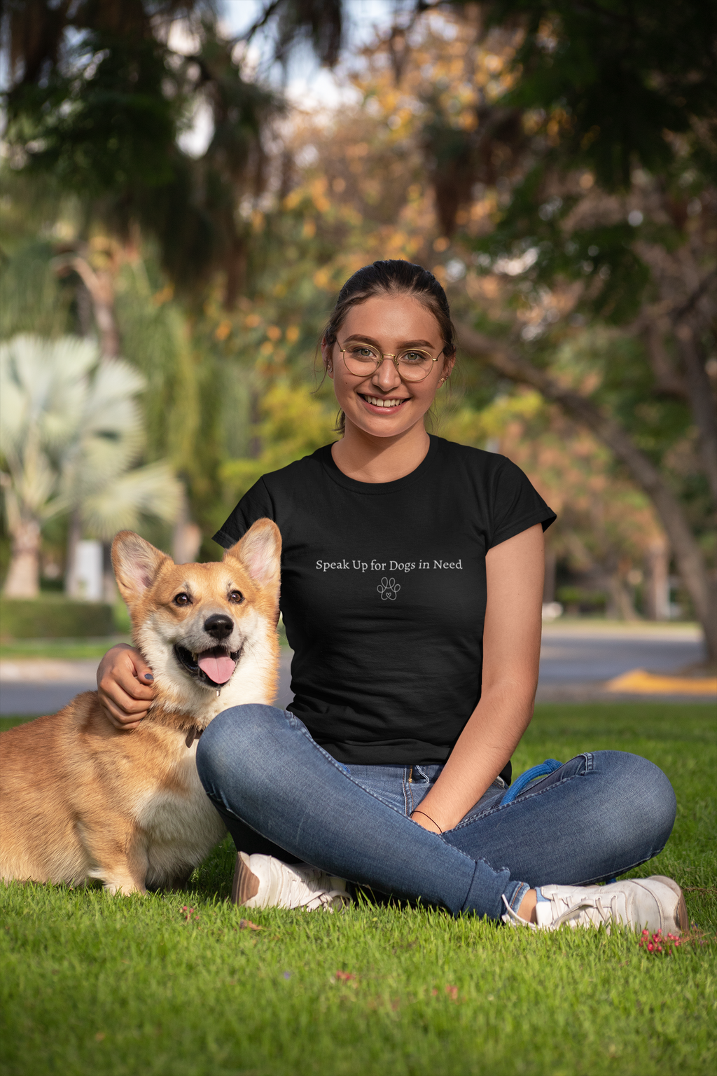 Woman sitting on grass with a dog, wearing a black t-shirt with 'speak up for dogs in need' text.