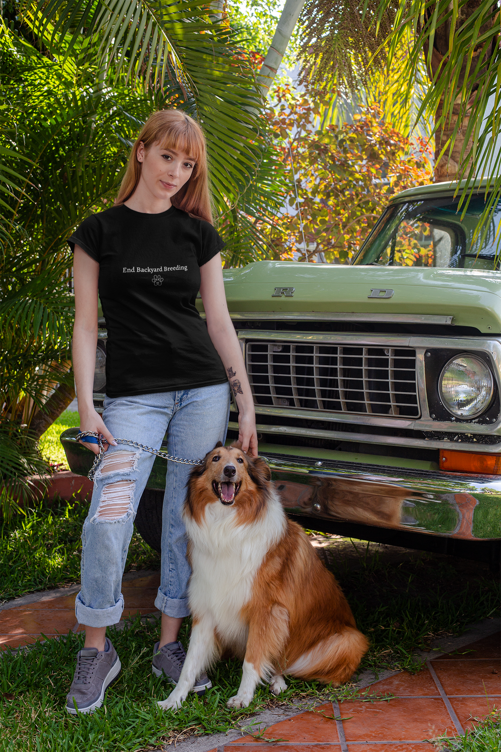 Woman in black t-shirt and jeans standing with a dog in front of a vintage truck.