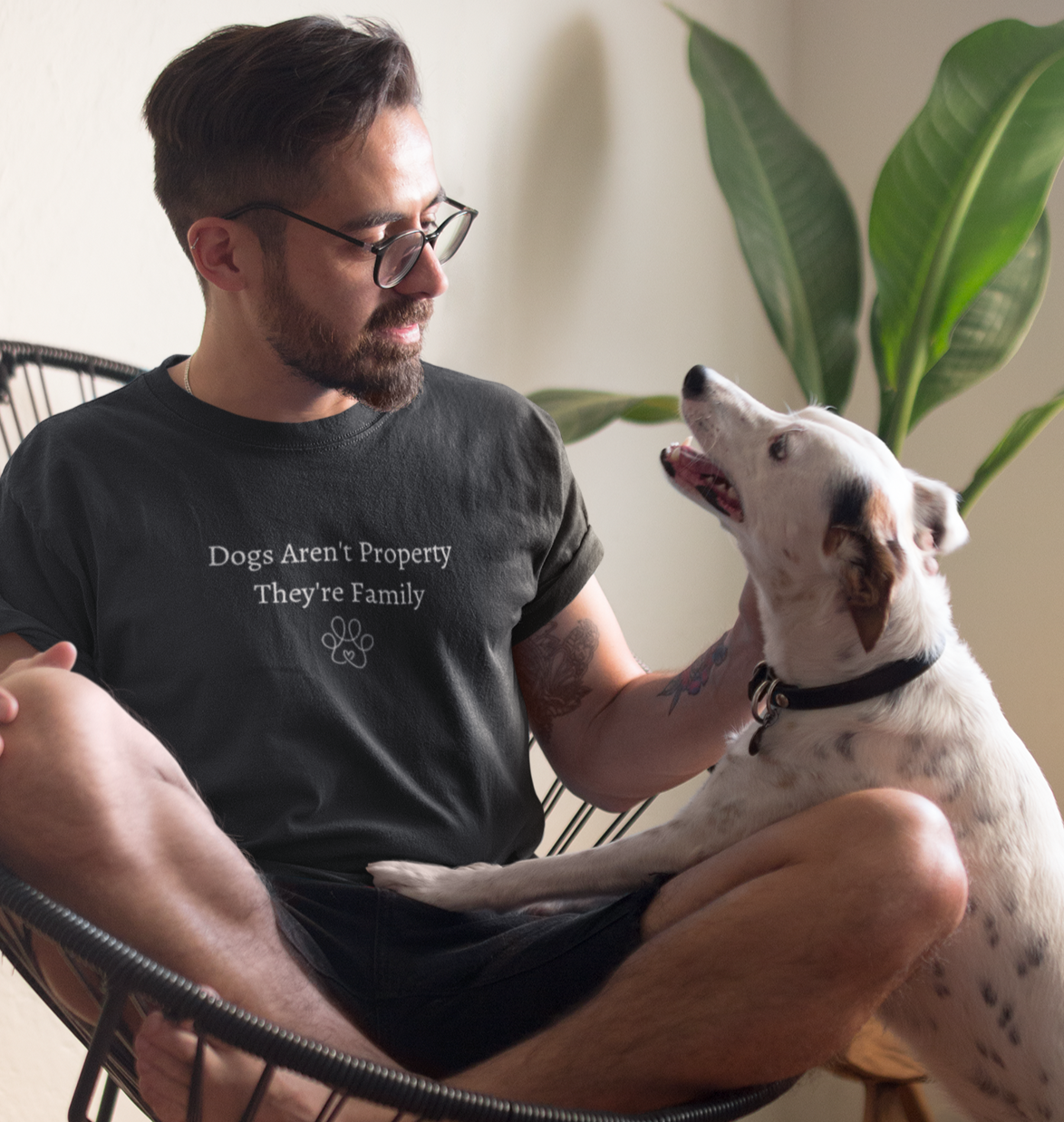 Man sitting on a chair with a dog, wearing a t-shirt with a message about dogs.